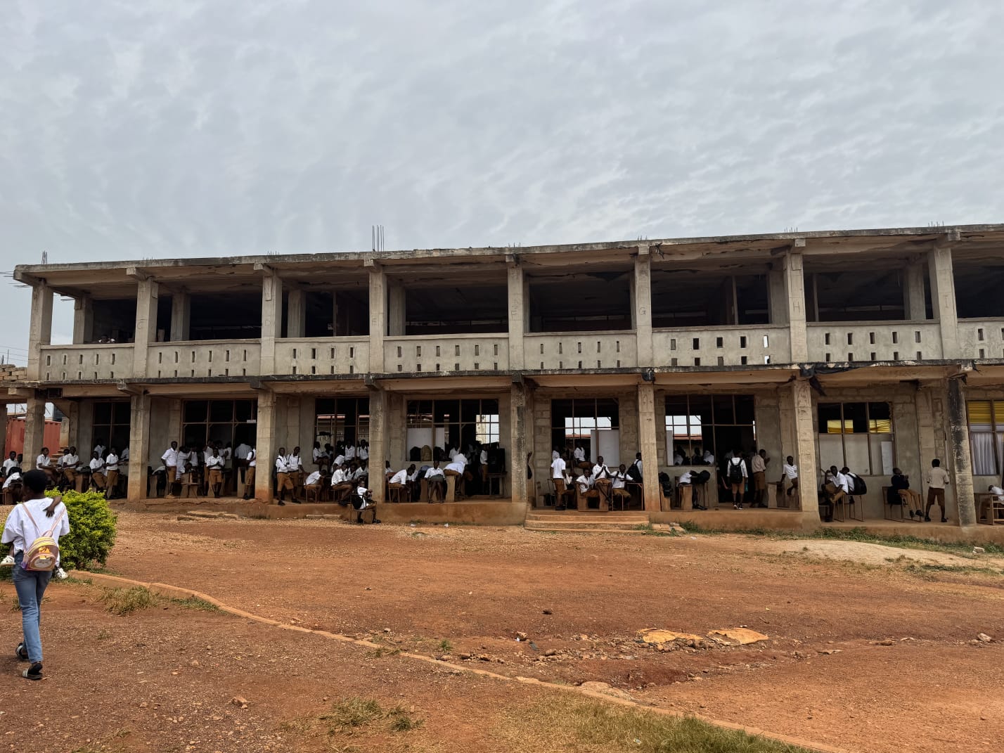Two-storey school building with students in classrooms and a learner walking across the compound