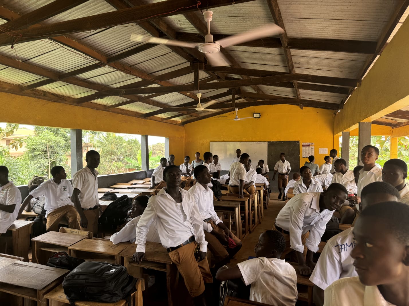 A full classroom of senior high students in white shirts turning towards the camera