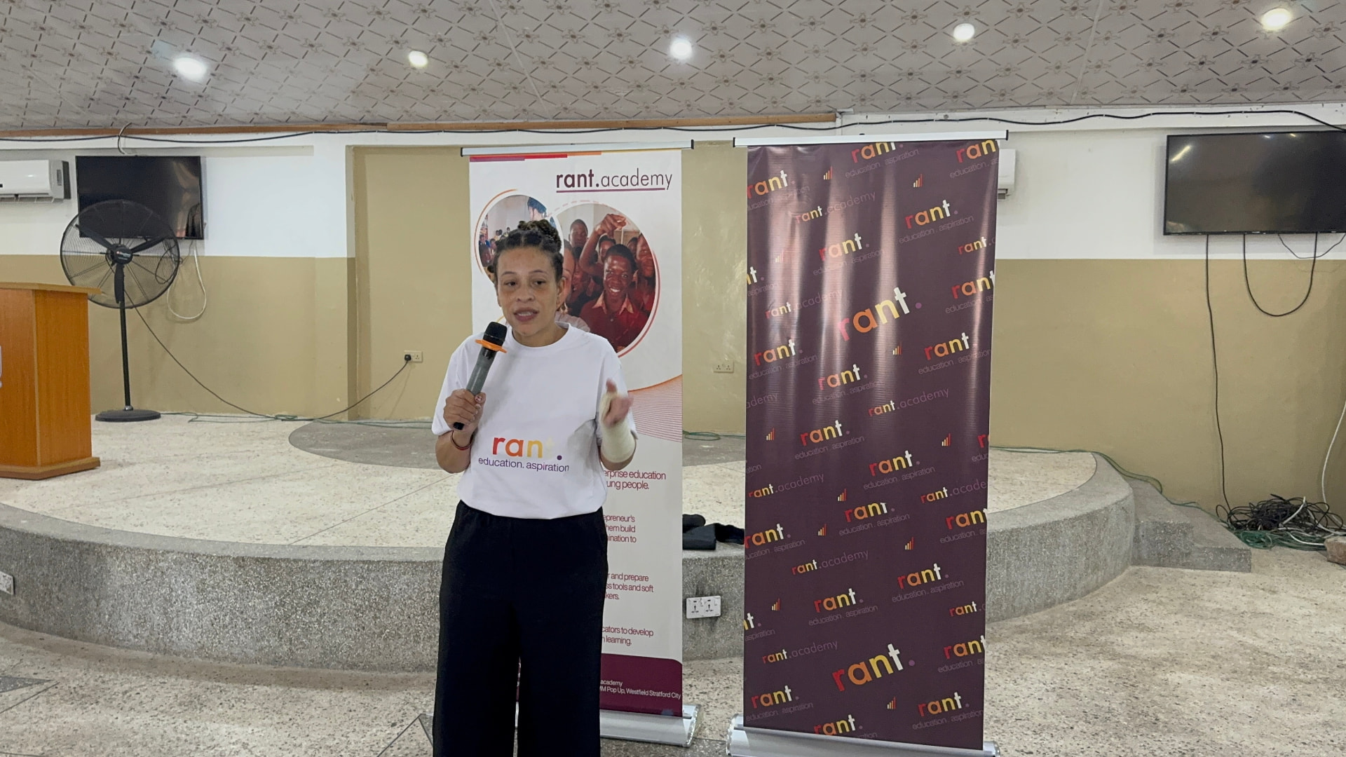 RANT facilitator addressing a room with a microphone in front of RANT Academy banners