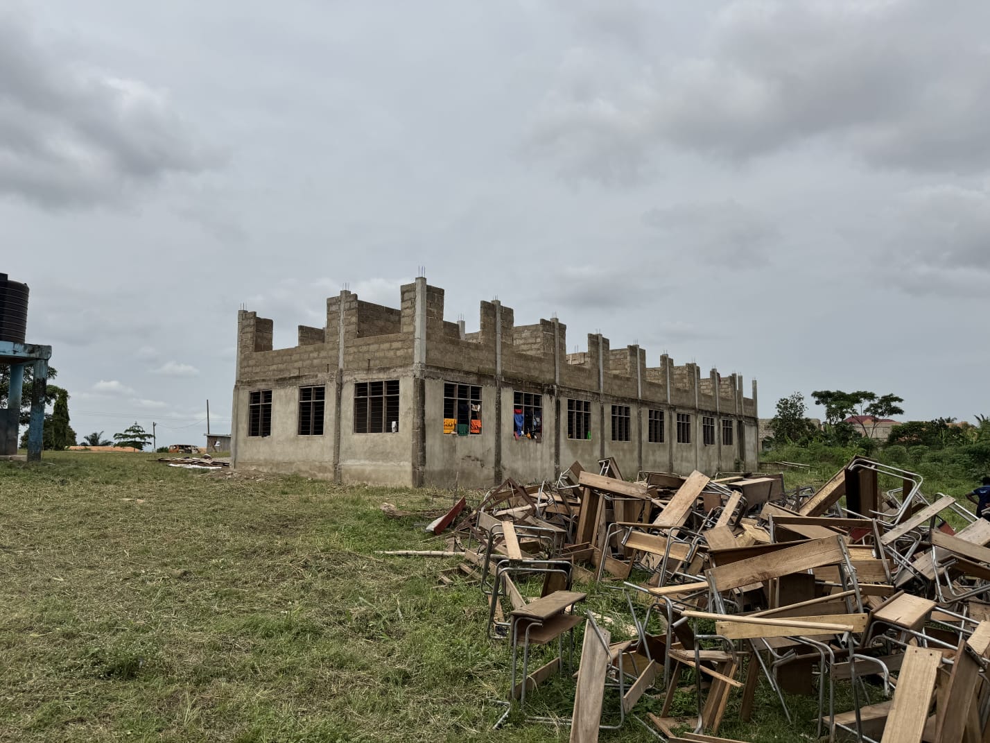 Unfinished school block with stacked wooden desks on the grounds