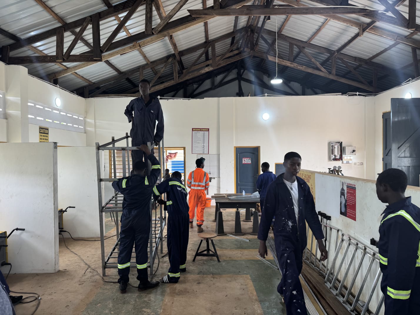 Trainees in overalls assembling a metal frame in a technical institute welding workshop